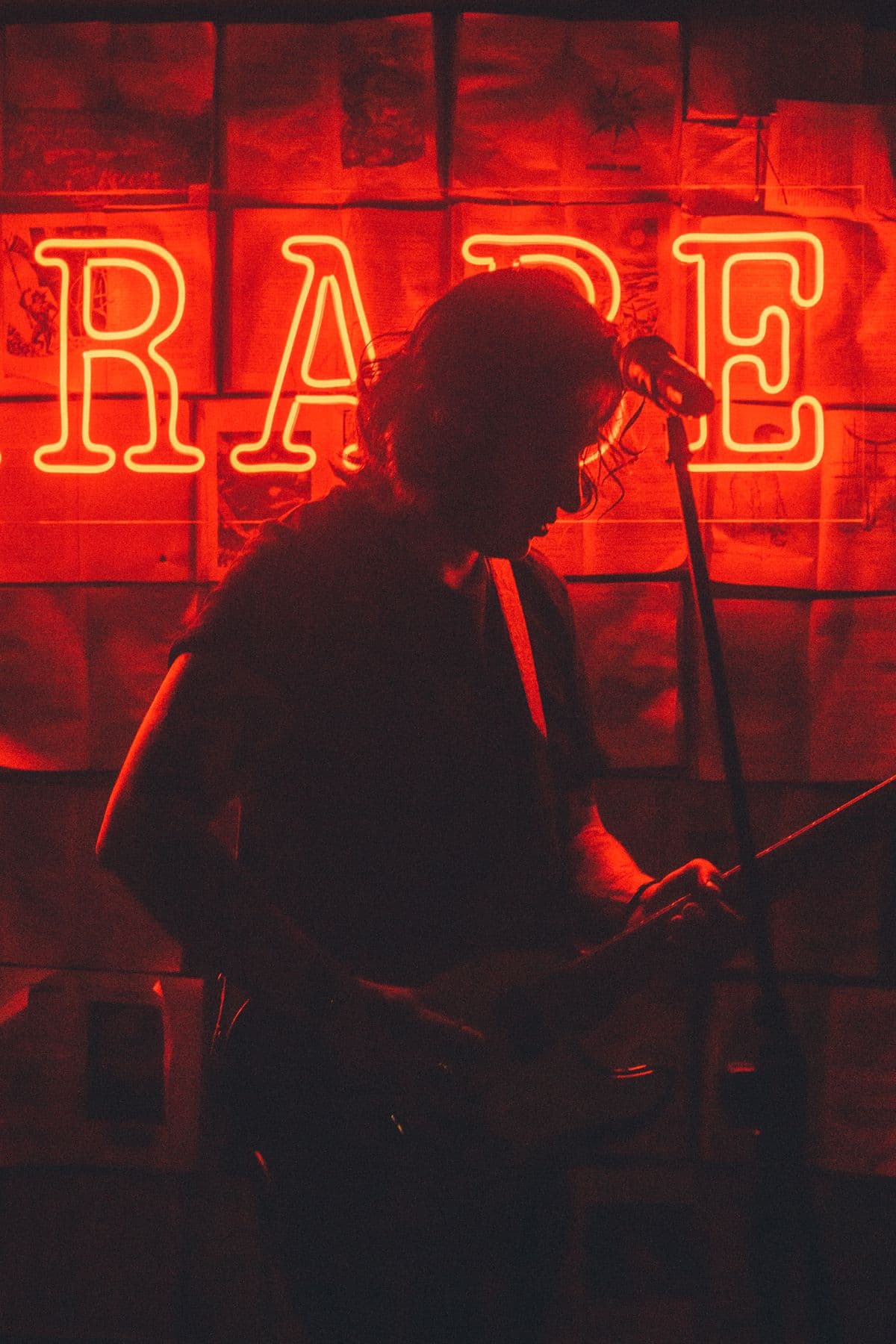 Silhouette d'un chanteur sur scène devant une enseigne au néon rouge, de nuit